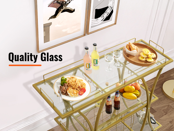 gold metal and glass VEVOR bar cart with food and drinks, against a white wall with framed pictures.