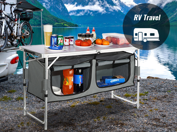 rv travel setup with a VEVOR camping table, filled with groceries, next to a scenic lakeside mountain view.
