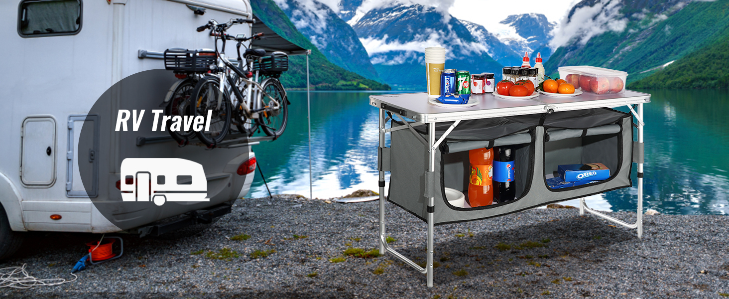rv travel setup with a VEVOR camping table, filled with groceries, next to a scenic lakeside mountain view.