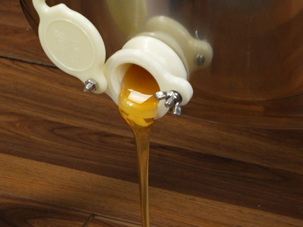 honey flowing from VEVOR electric honey extractor into a glass jar on wooden floor.