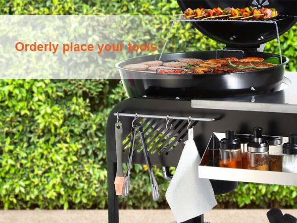 VEVOR charcoal grill with tool hooks, spices, and grilled food against a green hedge backdrop.