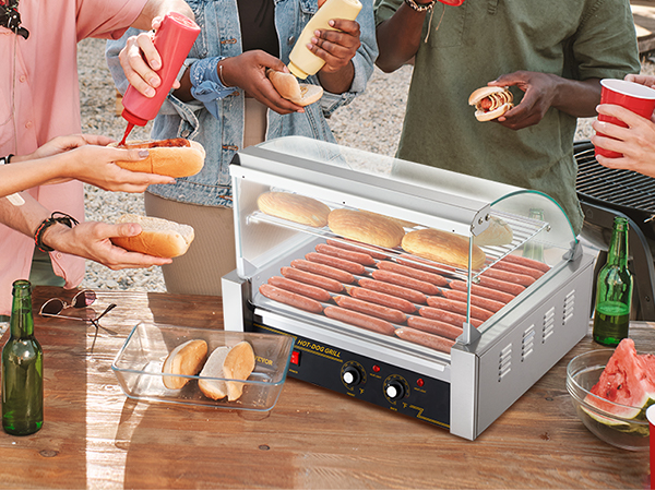 Draugi bauda hotdogus ar VEVOR hotdogu rullīti brīvdabas pulcēšanās laikā.