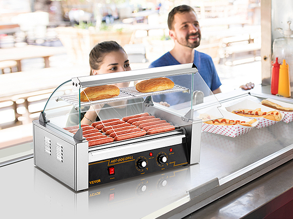VEVOR hotdogu rullis ēdienu stendā ar gatavotiem hotdogiem, maizītēm uz plaukta un apkalpotāju, kas pieņem pasūtījumus.