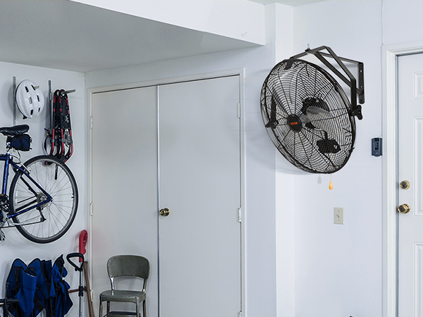 garage with mounted bicycles, folded chairs, and a VEVOR wall mount fan on a white wall near the door.