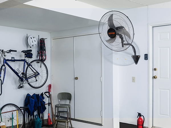 гараж с настенным вентилятором VEVOR, велосипедами, металлическим стулом и ящиками для хранения вещей у белой стены.