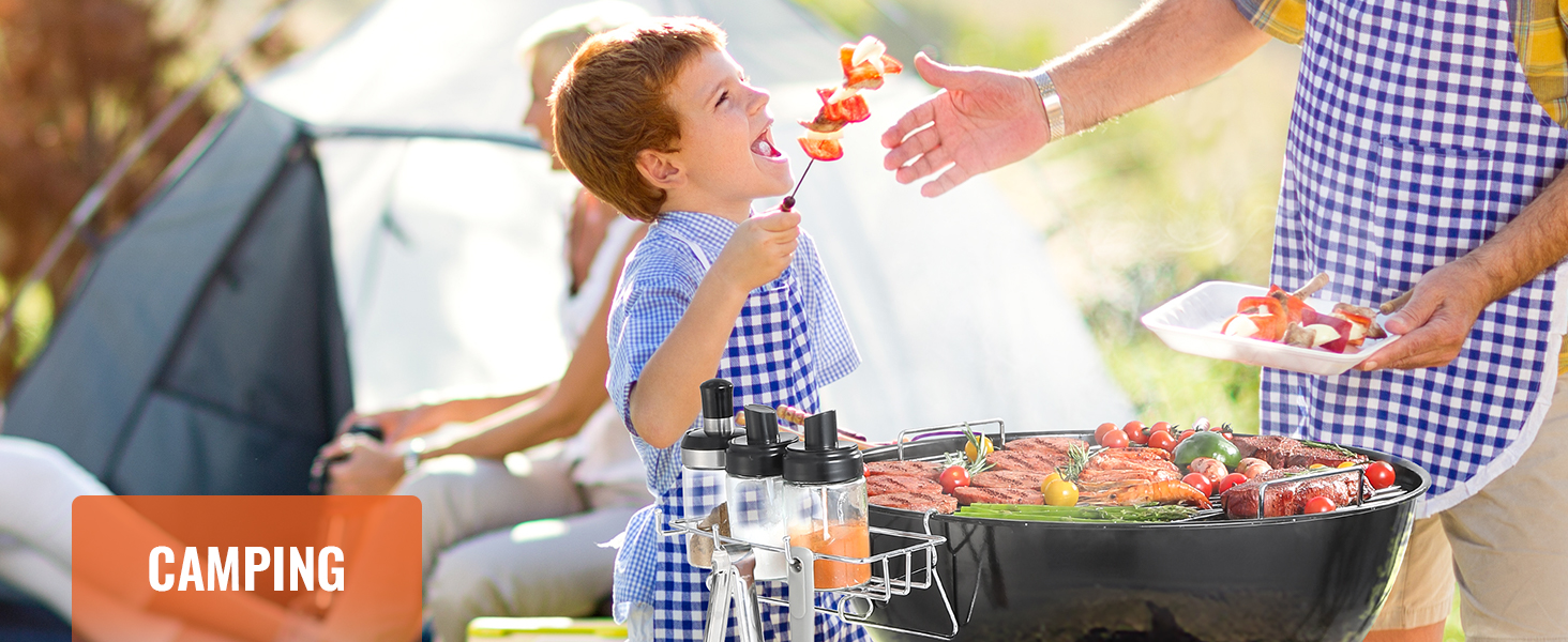 Kempinga grila aina ar ģimeni un VEVOR gatavošanas restēm, iesmu, garšvielām un grilētiem dārzeņiem.