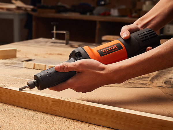 carpenter using VEVOR die grinder to sand a wooden plank in a workshop surrounded by tools and wood shavings.