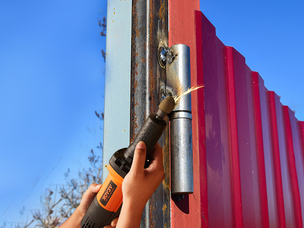 person using VEVOR die grinder to grind a metal piece attached to red metal panels on a sunny day.
