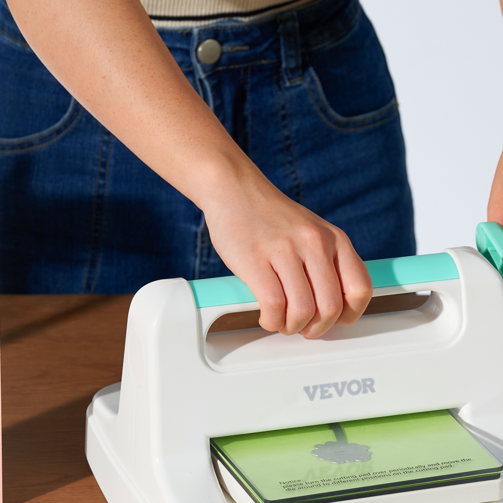 person using VEVOR die cutting machine with blue handle and green cutting mat. denim jeans background.