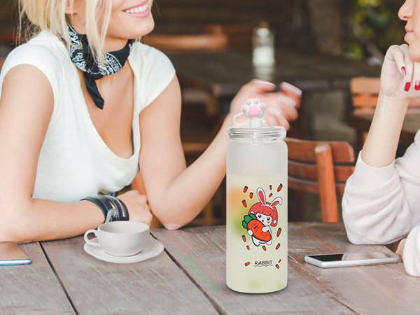 dvi moterys kalbasi prie stalo su cute rabbit tematikos vandens butelį ir išmaniųjų telefonų.