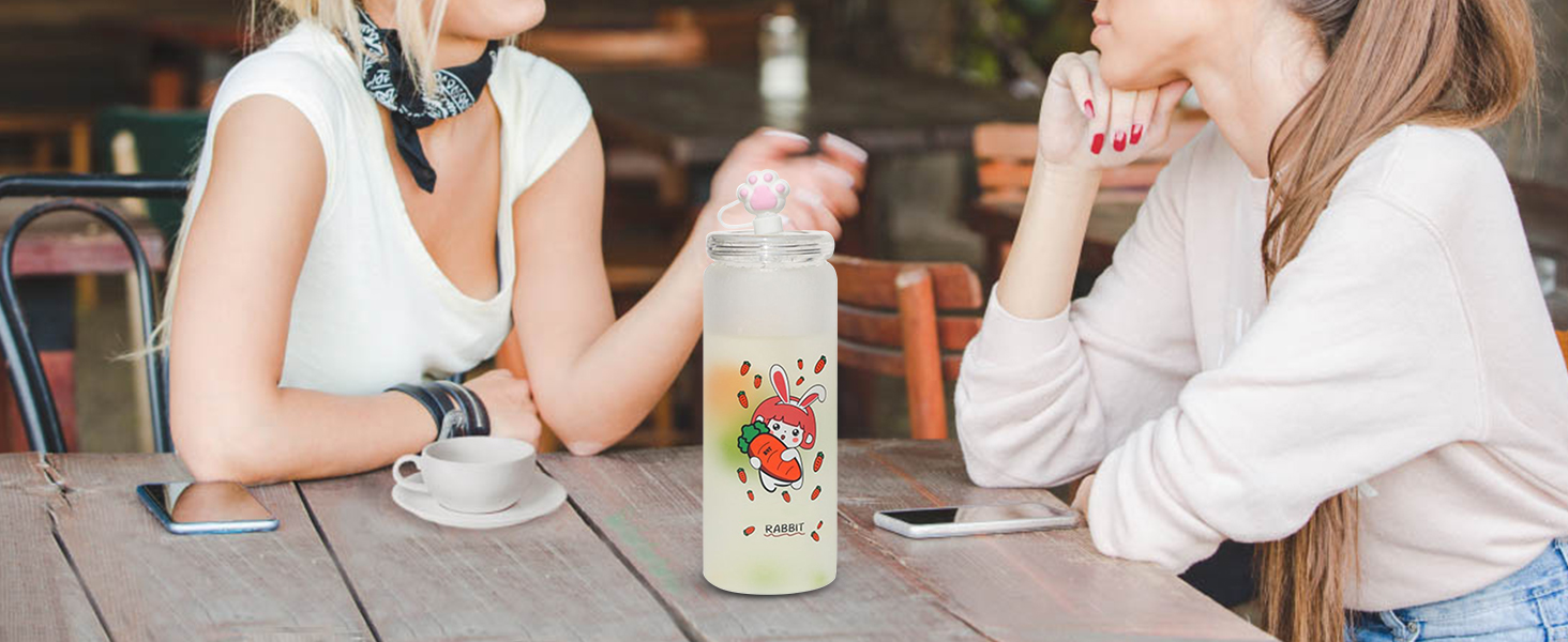 dvi moterys kalbasi prie stalo su cute rabbit tematikos vandens butelį ir išmaniųjų telefonų.