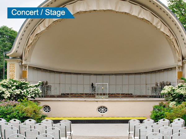 Āra koncerta skatuves iekārtojums ar krēsliem, kokiem un VEVOR kabeļu aizsargrampu pie skatuves.