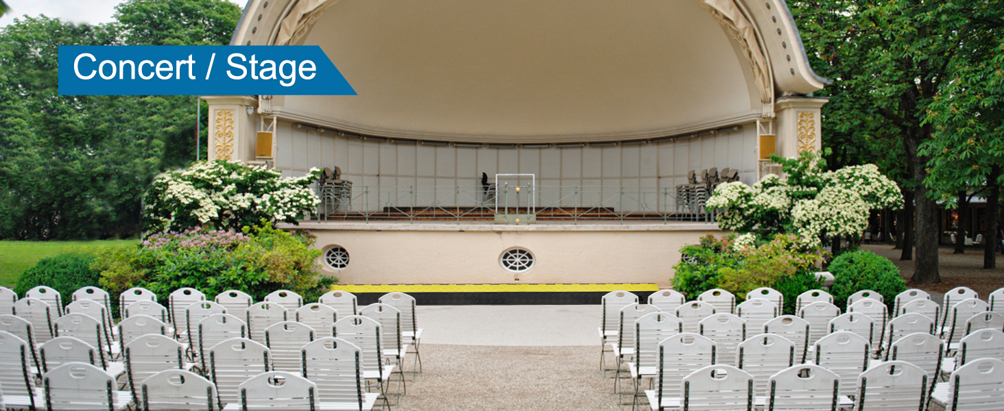 Āra koncerta skatuves iekārtojums ar krēsliem, kokiem un VEVOR kabeļu aizsargrampu pie skatuves.