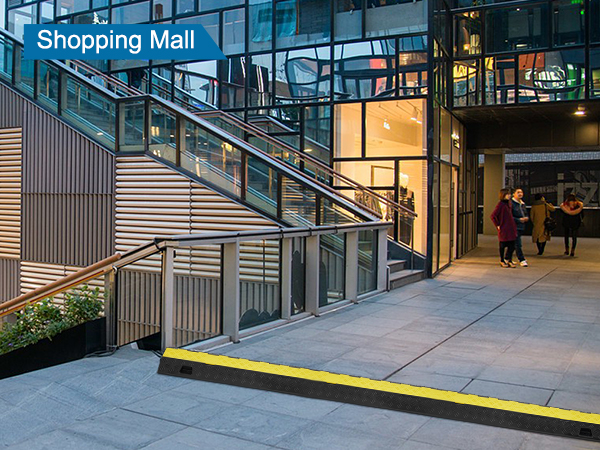 VEVOR kabeļu aizsargrampa pie iepirkšanās centra ieejas ar kāpnēm un mazumtirdzniecības veikalu fonā.