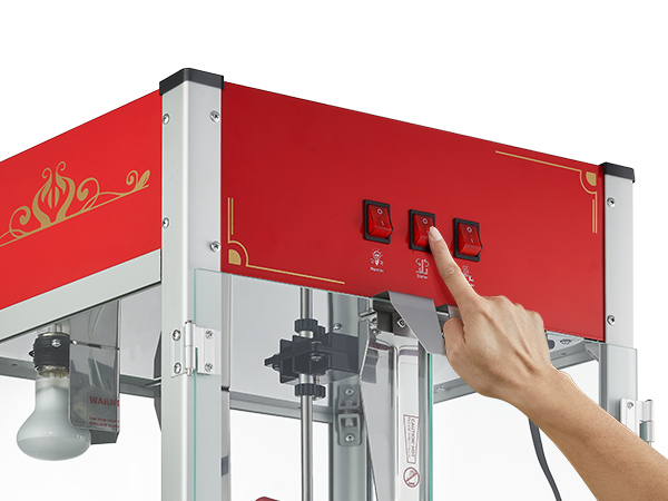 hand operating the red control panel of a VEVOR popcorn popper machine with switches.