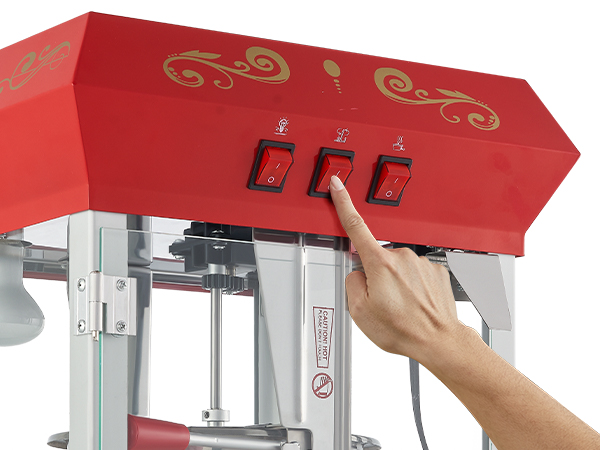 hand operating the red VEVOR popcorn popper machine with intricate gold designs and three control switches.