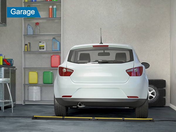 white car in a garage with VEVOR cable protector ramp near rear tires, workbench and storage shelves in view.