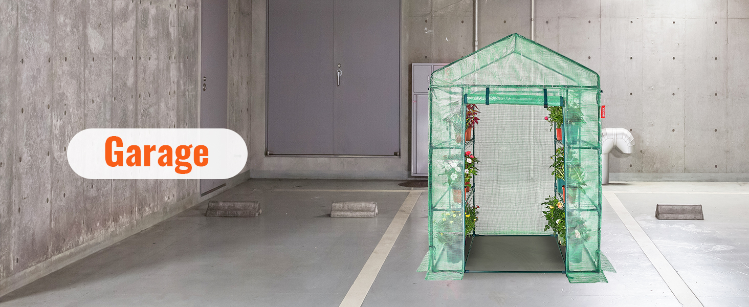 VEVOR walk-in greenhouse in a concrete garage, filled with potted plants along the sides.