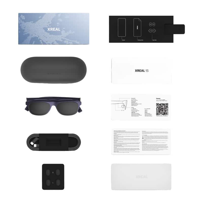 XREAL product kit laid out: blue world-map box on top left and black accessory insert on top right, with a matte black charging case and sunglasses below. Next to white XREAL 1S box and various instruction sheets with a QR code.